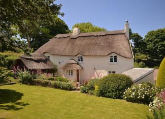 Large thatched cottage overlooking a large lawn fringed with flowering shrubs.