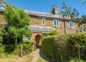 A footpath flanked by privet hedges leads to a stone-built holiday cottage with a covered porch