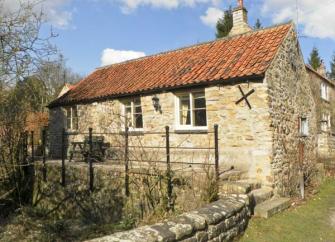 A single storey stone built cottage with a raised terrace overlooking a garden.