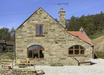 A stone-built North Yorkshire holiday cottage surrounded by woods and fields.