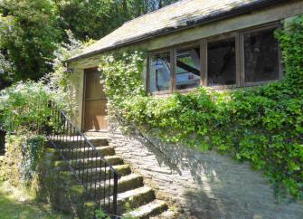 The leafy-clad exterior of a stone-built single-storey exmoor holiday cottage with a flight of stone steps to the front door.