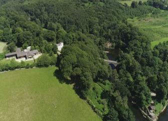 Aerial photo of a large holiday home nestling between mature woodland and fields overlooking a wide river.