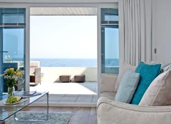 A lounge with comfortable sofas and TV has French windows with a sea view