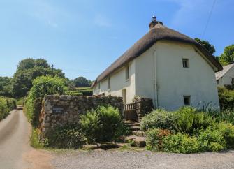 Exterior of a large thatched Dartmoor farmhouse amidst mature gardens