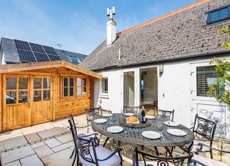 A single-storey holiday cottage overlooks a courtyard with a table laid for a meal