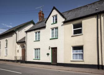 Eterior of a double-fronted terraced cottage overlooking an empty village street.