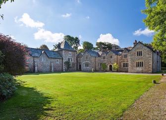 A sprawling Dartmoor Manor house ovrlooks a sweeping, tree-lined lawn.