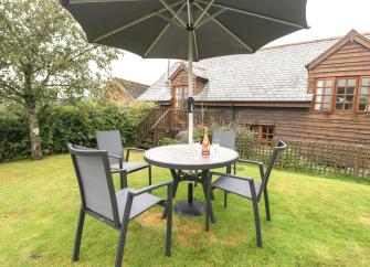 A wooden holiday cottage overlooks a large lawn with outdoor dining furniture.