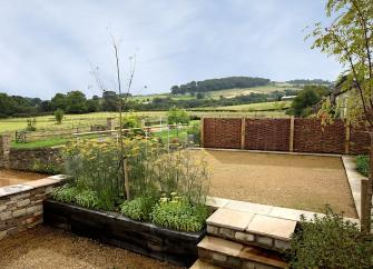 A cottage garden with rural views of hills and open countryside beyond a hedge.