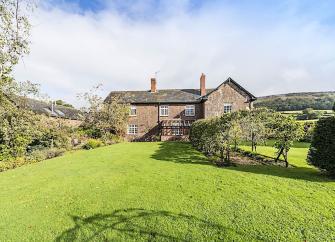 A stone cottage surrounded by fields overlooks a large garden with apple trees.