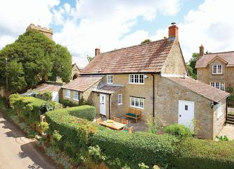 A semi-detached, stone-built village cottage surrounded by a privet-hedged garden.