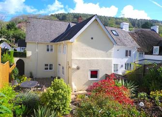 Exterior of a Devon village cottage with a patio and a well-kept garden.