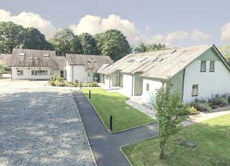 Large slate-roofed, Lake District lodges with front lawns overlooking a shingled courtyard.