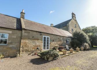 A siingle-storey stone-built cottage with French windows opening onto a paved courtyard.