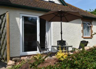 Exterior of a chalet bungalow with a courtyard containing a table with a parasol and chairs.