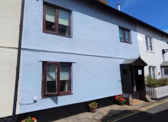 A 2-storey holiday cottage in Watchet with a gabled porch opening onto a village street.