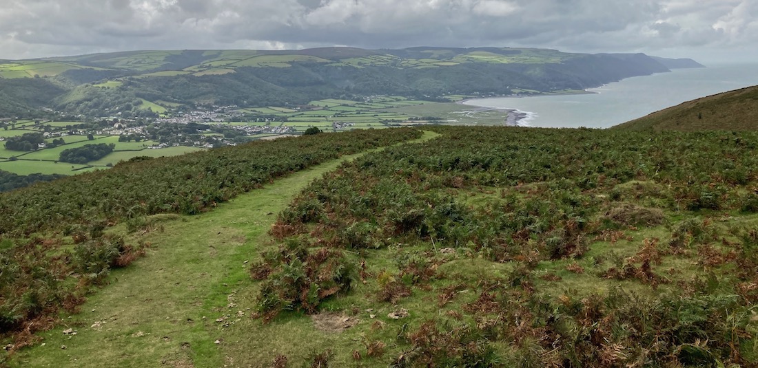 Exmoor landscape view of Porlock Vale from Selworthy Beacon. A hilltop view of the coast with a small village nestling between the hills overlooking the coast.