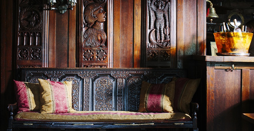 An ornately carved wooden settle sits in front of an equally well-carved oak panelling.