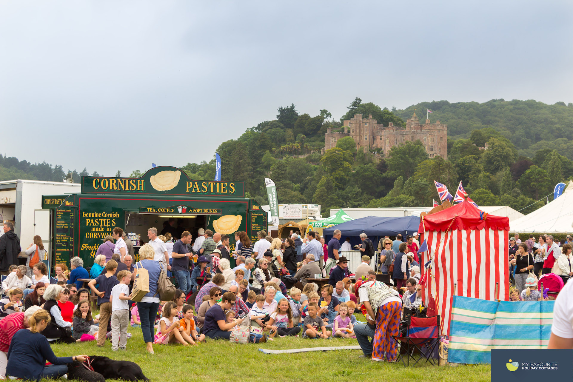 A punch and judy show at a country fair overlooked by Dunster castle