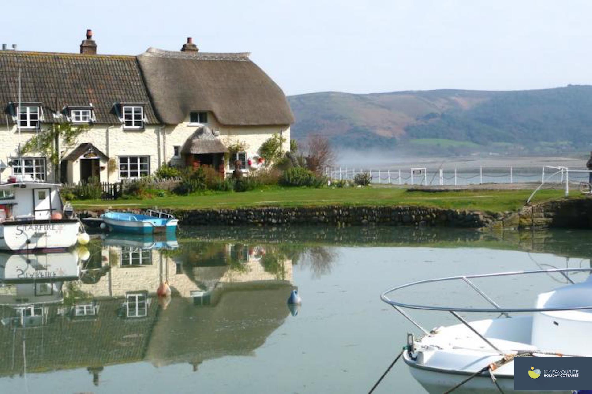 a thatched holiday cottage in Porlock Weir over looks a small harbour with a few boats ar moored.