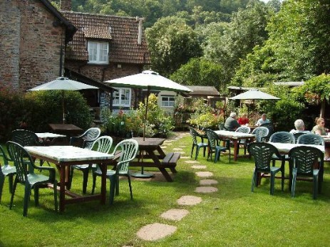 exterior and garden of an exmoor tearooms. Inthe background is  house and  tables tables with parasols and chairs are laid out in the lawned garden.