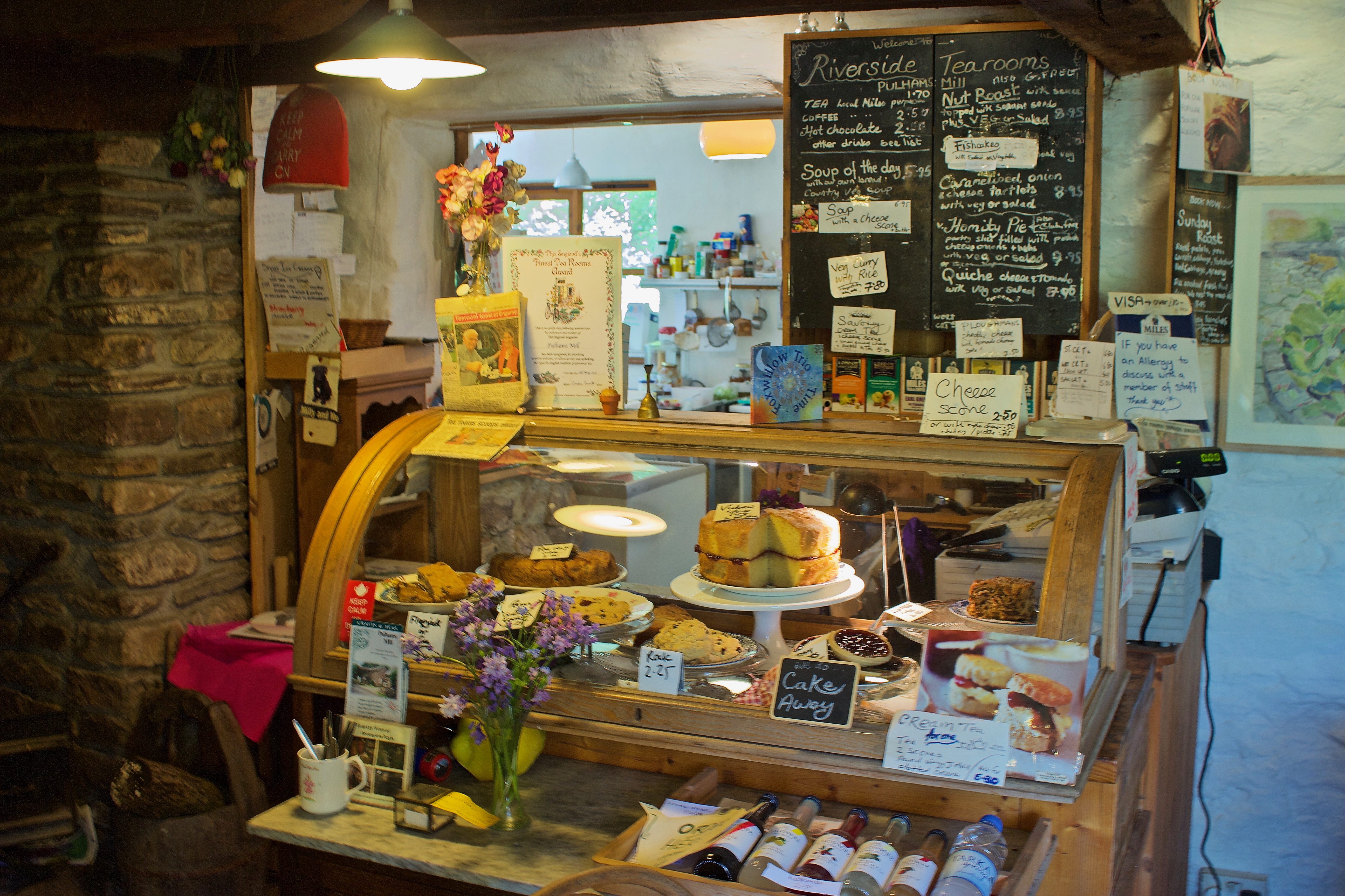 A display cabinet in an Exmoor tearooms featuring a range of scones,cakes, breads and pies. In the background are menu boards and price lists 