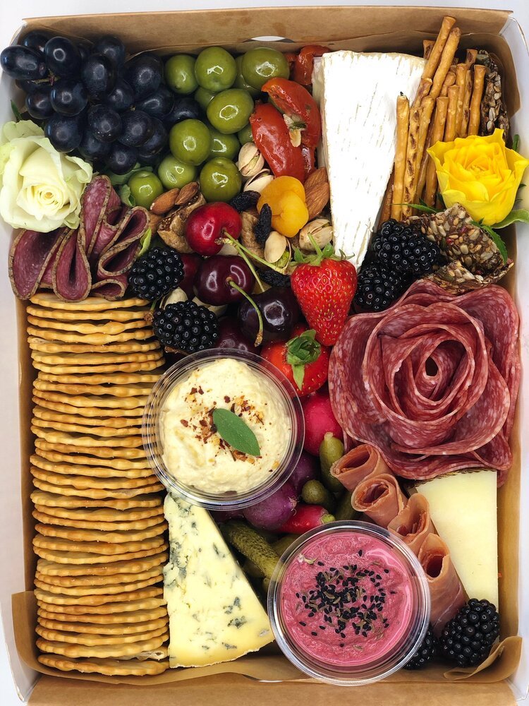 Looking down on a food box of biscuits, tarts. olives, yoghurt and blackberries
