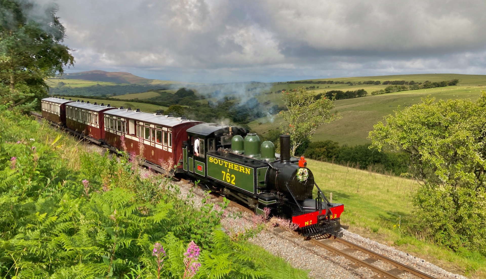 a narrow-gauge steam engine and three carriages steams through open countryside on Exmoor