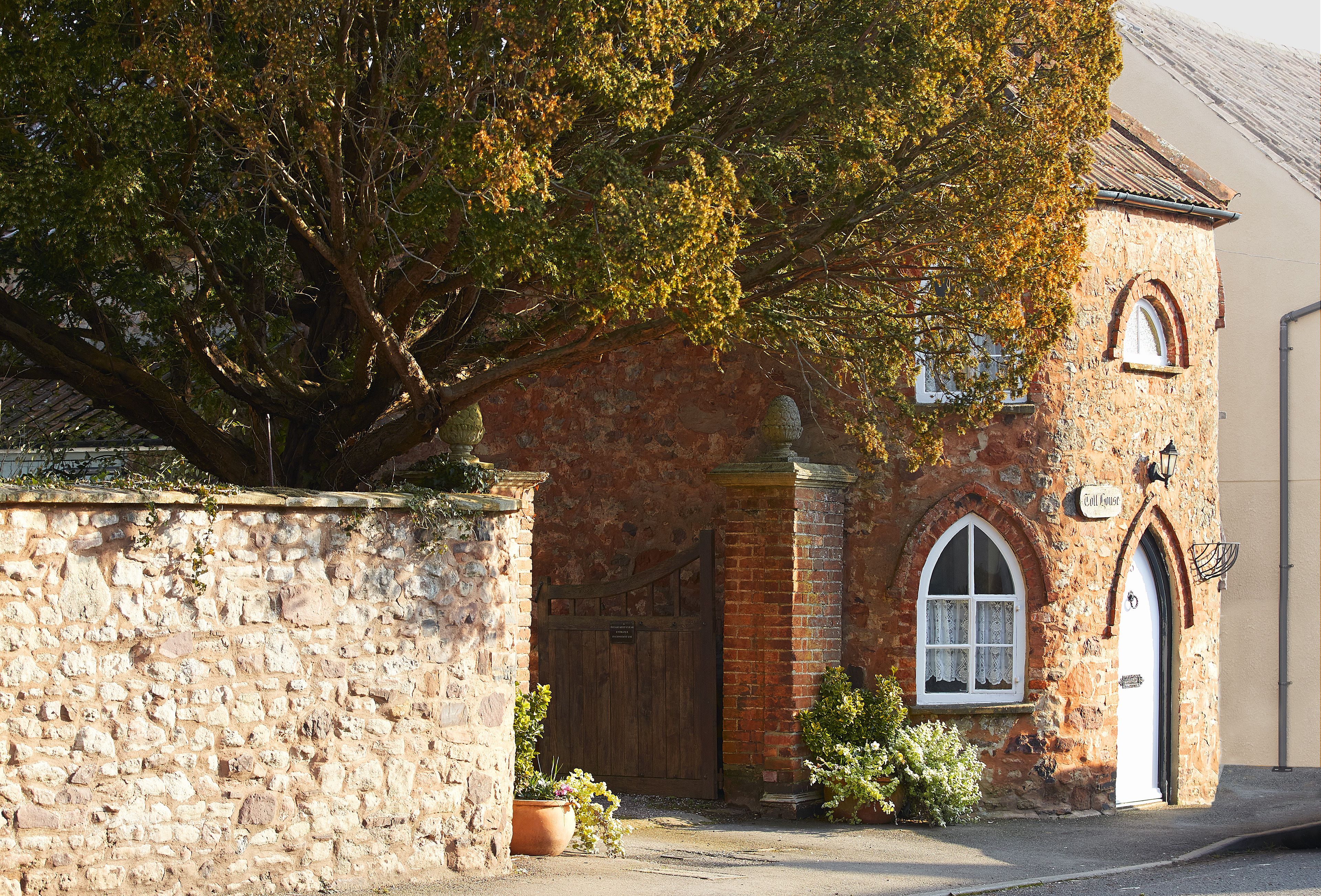 An old tollhouse with arched windows and front door basks in the afternoon sunshine in Nether Stowey.