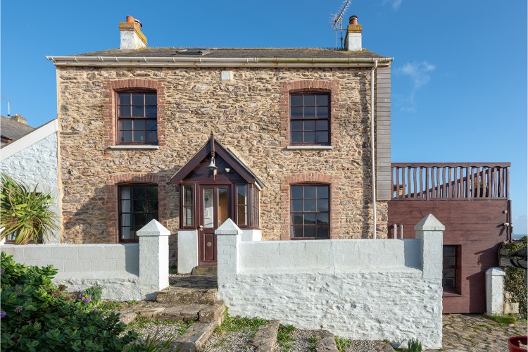 A double-fronted Portwrinkle cottage with whitewashed front garden walls and covered porch..