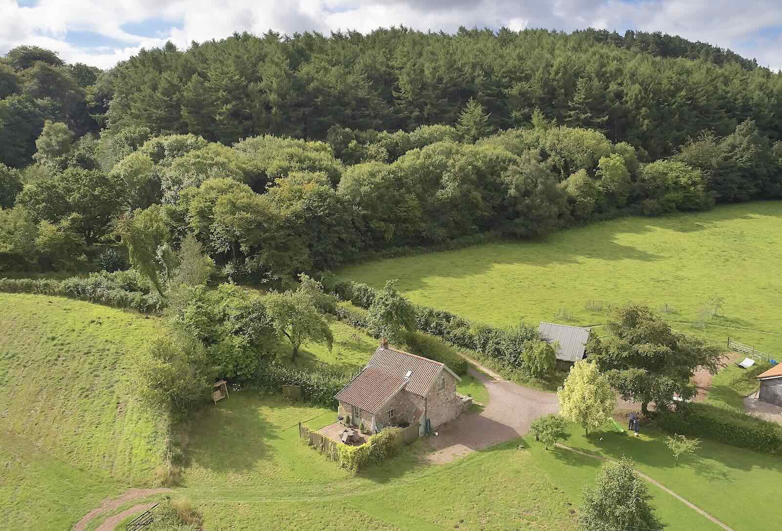 An aerial view of a stone-built Wye Valley cottage surrounded by fields and  dense woodland on a sunny day.