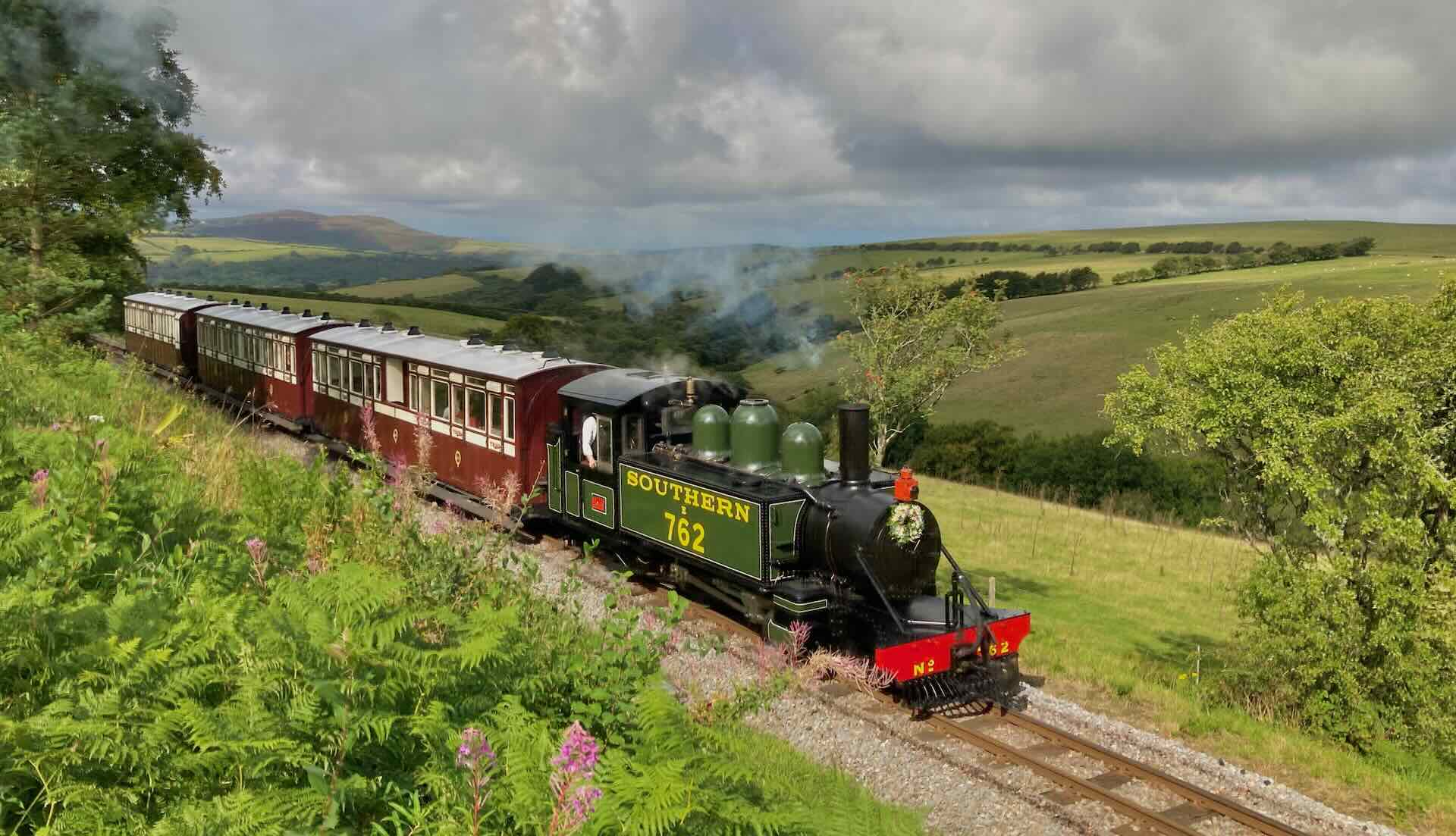 a narrow-gauge steam engine and three carriages steams across Exmoor countryside