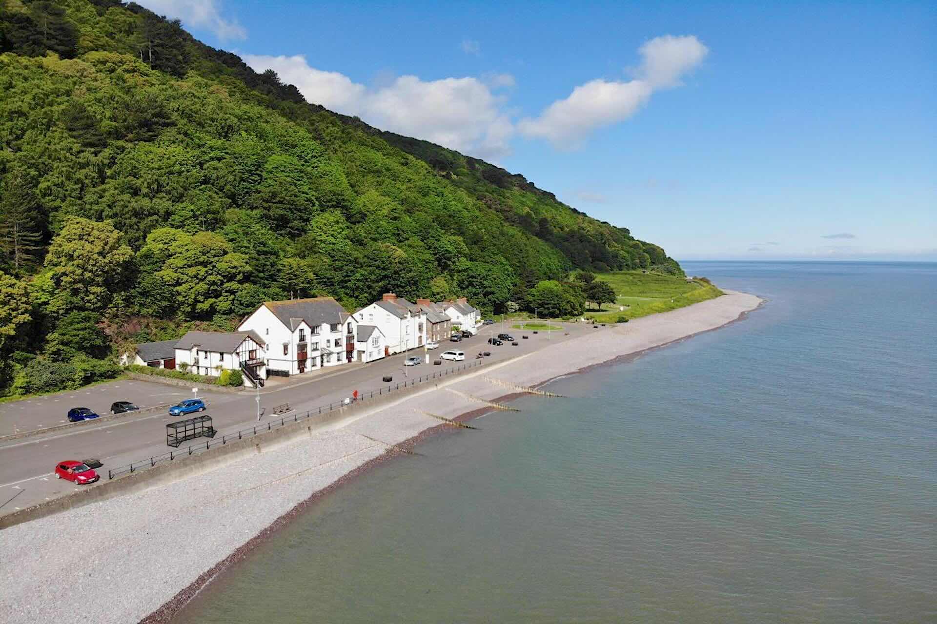 Holiday cottages on the Exmoor Coast nestle just above the shoreline beneath a steep, wooded hill.