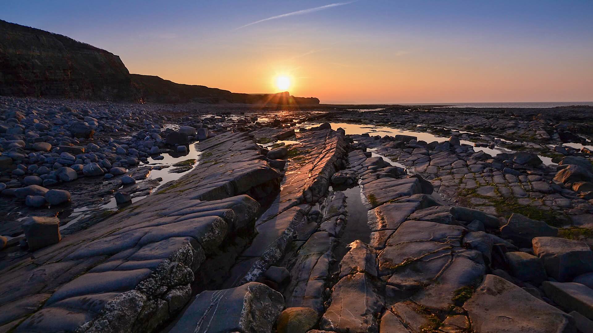 A summer sunset on Kilve beach at low tide reveals rows of jagged rocks.