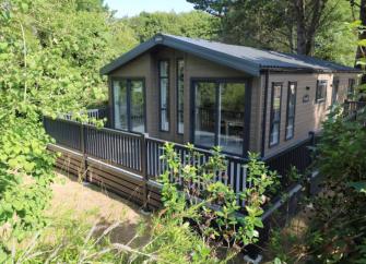 A static caravan with a fenced in dack is surrounded by trees and bushes