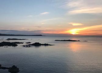 Sunset over The Moray Firth, a calm sea reflecting the sinking sun with tiny rocky islands silhouetted against the darkening sky.