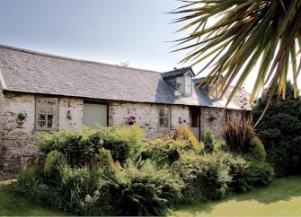A North Devon coast stone-barn conversion overlooking. lawned garden with a palm tree
