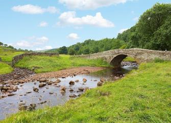 A single-arch stone bridge crosses a meandering river in Coverdale.