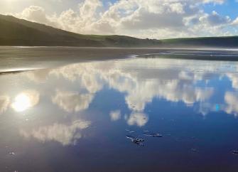 The sky and clouds are reflected in the wet sand on Woolacombe Beach.