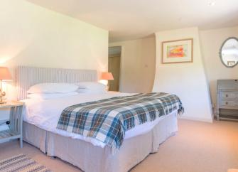 A spacious Bridport holiday cottage bedroom with a large double bed, tartan bedspread and carpeted floor.