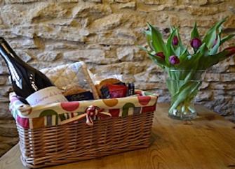 A North Yorkshire holiday cottage welcome basket stocked with goodies - bread, wine, jam, biscuits sits on a table. 