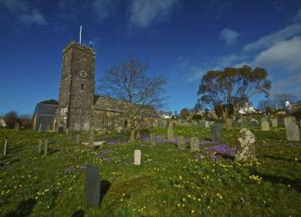 A North Devon hilltop church overlooks a grave yard filled with daffodil and crocus blooms.