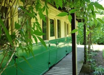 The exterior of restored railway carriage converted into self-ctering holiday accommodation with a vine-covered sun deck.