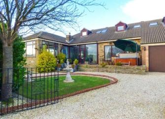 A large chalet bungalow with large glass windows and a hot tub on the front terrace.