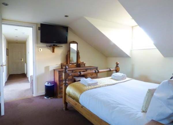 Double bedroom with bed, dressing table and wall-mounted TV.