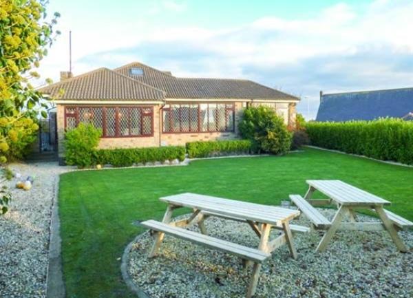 A hedge-lined lawn with a patio containing two picnic tables.
