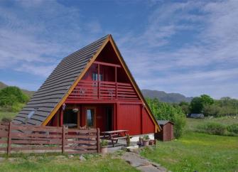 Exterior of a 2-storey, wooden A-Frame eco lodge surrounded by oprn countryside