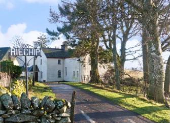 A tree-lined drive way curves toward a large rendered holiday home in Perthshire.