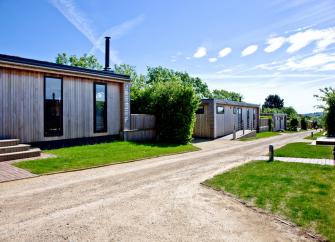 A single-storey wooden eco-lodge overlooks a lawn and drive.