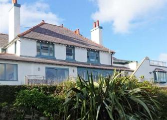 Exterior of a large holiday Anglesey holiday cottage with many windows and terrace overlooking a shrub-filled garden.